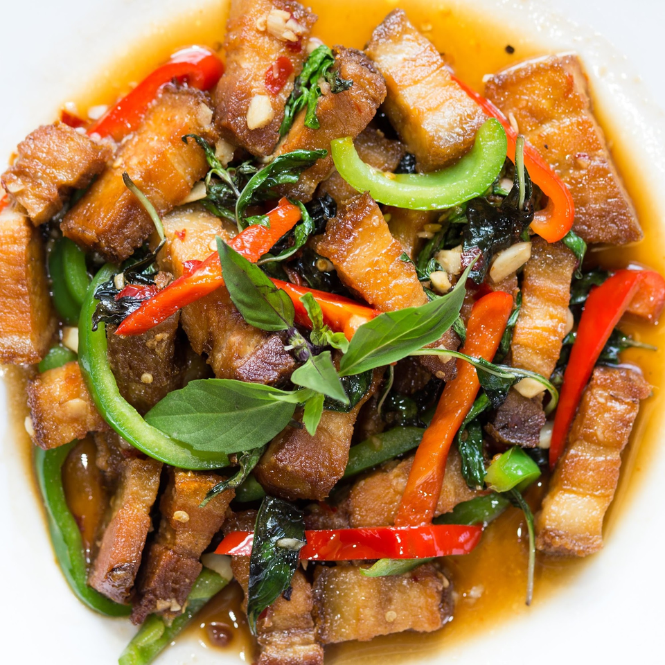 Close-up of crispy pork belly stir-fry with red and green bell peppers, basil, and garlic in sauce.